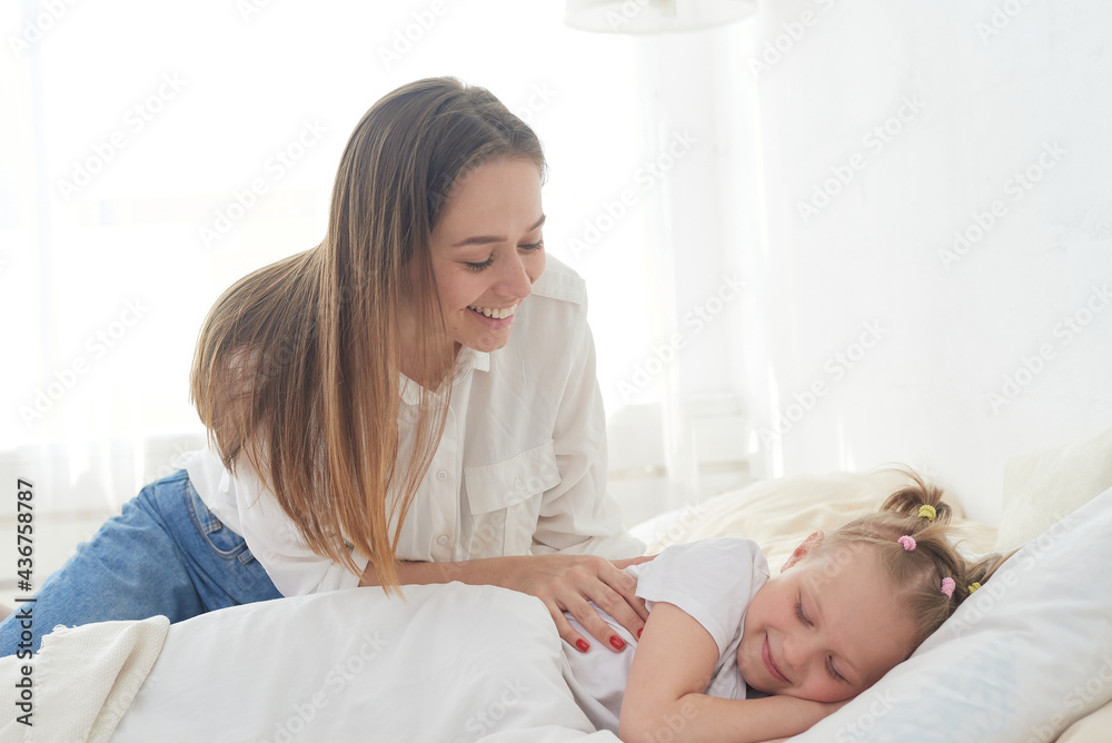 Beautiful young mom wakes up her preteen little daughter in the morning. Tenderness and care. Mother's love Beautiful young mom wakes up her preteen little daughter in the morning. Tenderness and care. Mother's love