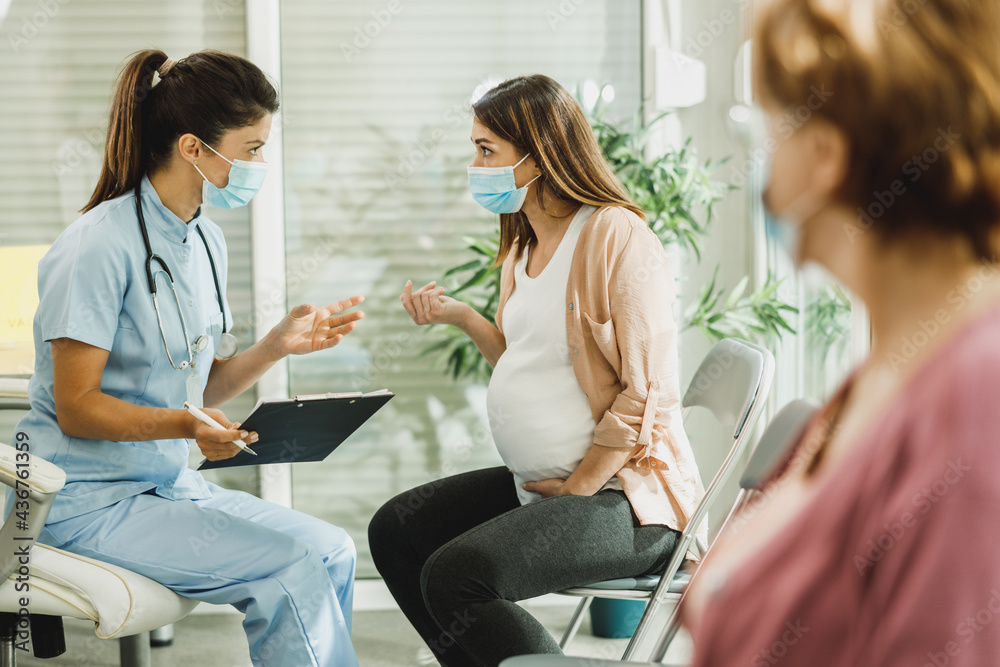 Obraz premium Pregnant Woman With Protective Mask Talking To Nurse At Waiting Room