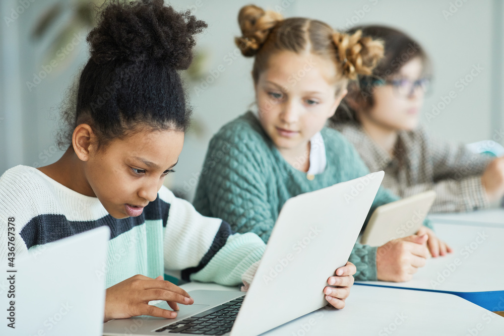Diverse group of children sitting in row at school classroom and using laptops Diverse group of children sitting in row at school classroom and using laptops