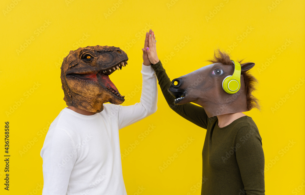 Excited couple of cheerful man and woman wearing dinosaur and horse head  mask giving high five.Friends lifestyle isolated over yellow background .  Stock Photo | Adobe Stock