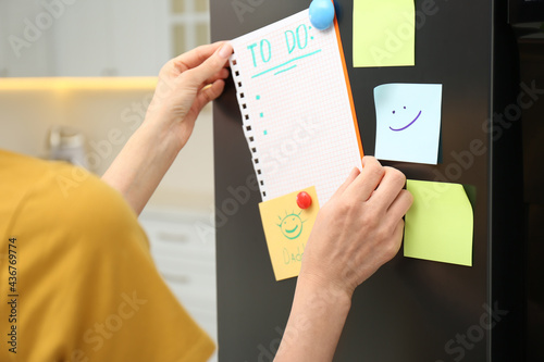 Foto Woman putting blank to do list on refrigerator door in kitchen, closeup