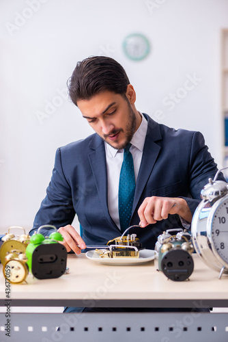 Young businessman employee eating alarm-clock