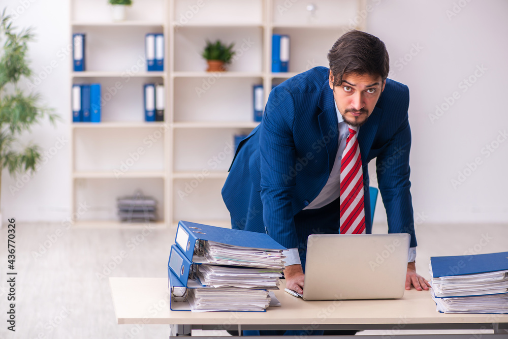 Young male employee unhappy with excessive work in the office Young male employee unhappy with excessive work in the office