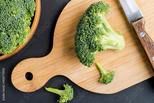 fresh green broccoli on wooden cutting board with knife on blue surface. Top of view