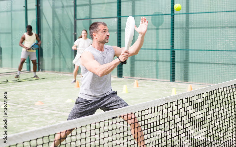 Man training to play tennis on the padel court outdoor. Athletes training in the background