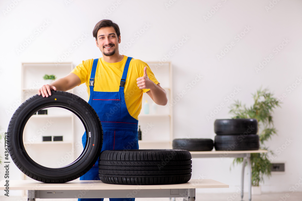 Young male garage worker with tyre at workshop Young male garage worker with tyre at workshop