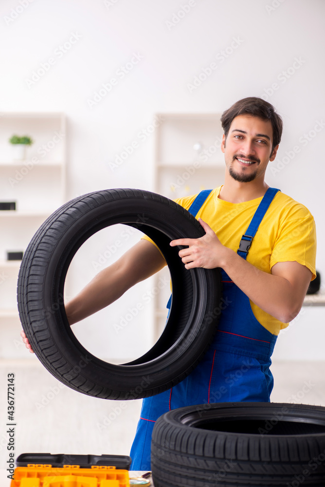 Young male garage worker with tyre at workshop Young male garage worker with tyre at workshop
