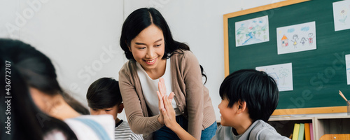 Young Asian teacher giving boy high five in school, success, achievement, happiness. Asia school boy with young woman in class.