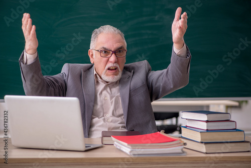 Old male teacher in front of blackboard