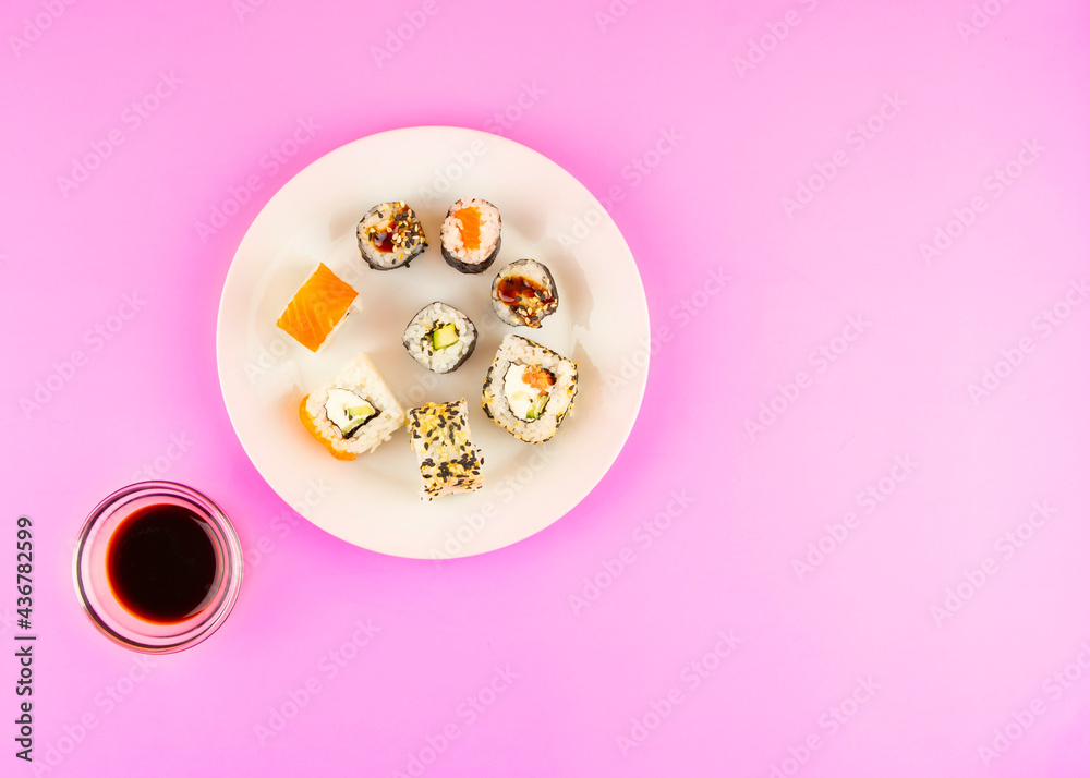 Composition of rolls on a white plate, soy sauce on a pink background. Asian food concept. View from above. Copy space Composition of rolls on a white plate, soy sauce on a pink background. Asian food concept. View from above. Copy space