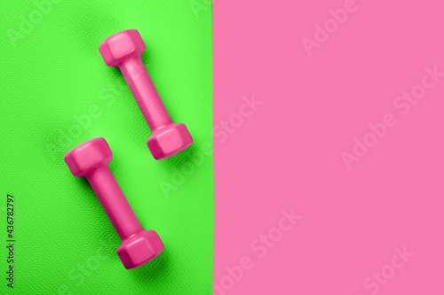 Top view of green sport mat and pink dumbbells neon pink background or set for pilates or fitness practice with copy space. Flat Lay. © greola84