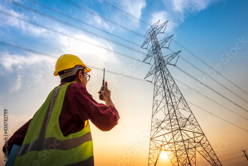 An electrical engineer standing and watching at the electric power station to view the planning work by producing electricity at high voltage electricity poles. photo