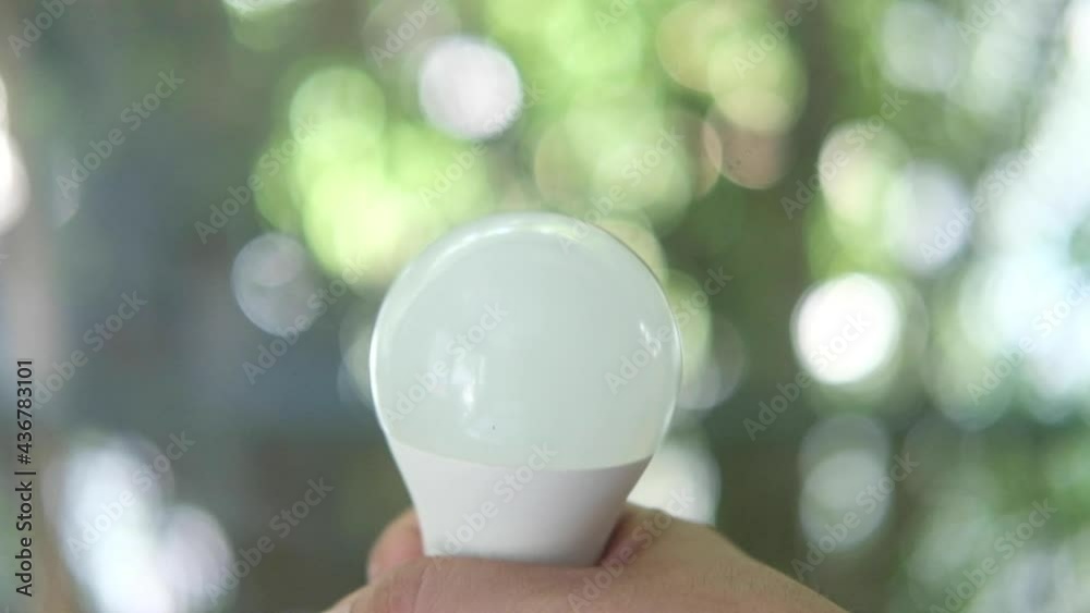 Male hand holds up LED light bulb with green nature background. Male hand holds up LED light bulb with green nature background.