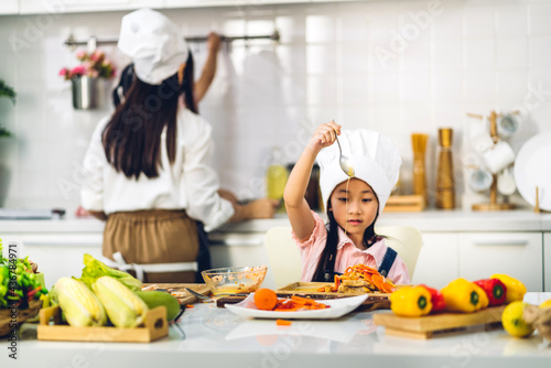 Portrait of enjoy happy love asian family mother and little asian girl daughter child having fun cooking together with fresh vegetable salad and sandwich ingredients on table in kitchen
