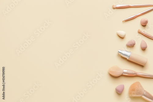 Makeup sponges with tonal foundation and brushes on color background
