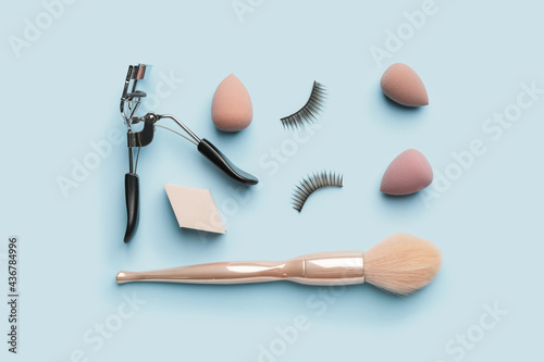 Makeup sponges with brush and eyelash curler on color background