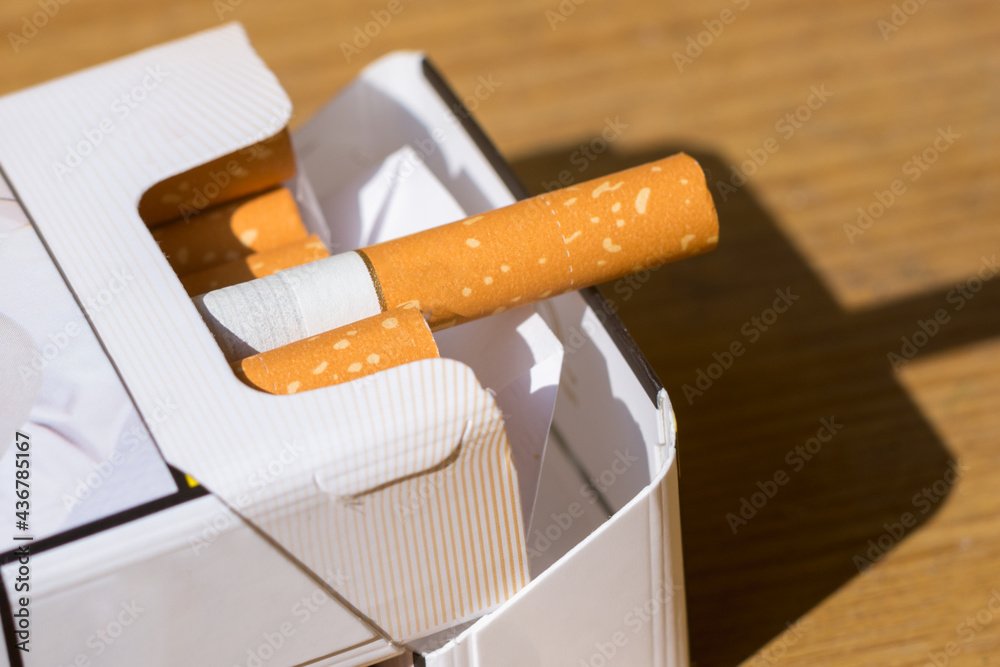 Open pack of cigarettes on old wooden table.Closeup pile cigarettes on a yellow table. Open pack of cigarettes on old wooden table.Closeup pile cigarettes on a yellow table.