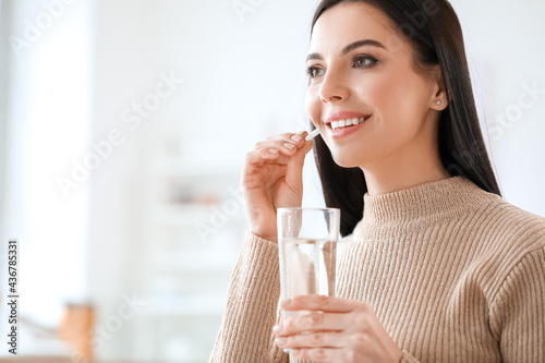 Beautiful young woman taking pills at home photo