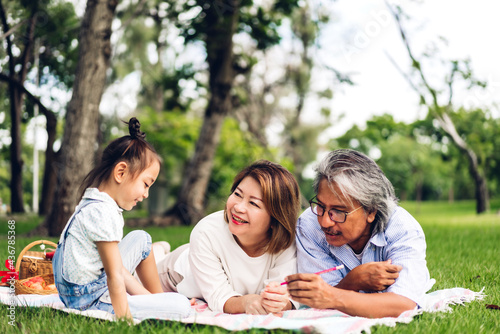Portrait of happy asian grandfather with grandmother and asian little cute girl enjoy relax in summer park.Young girl with their laughing grandparents smiling together.Family and togetherness
