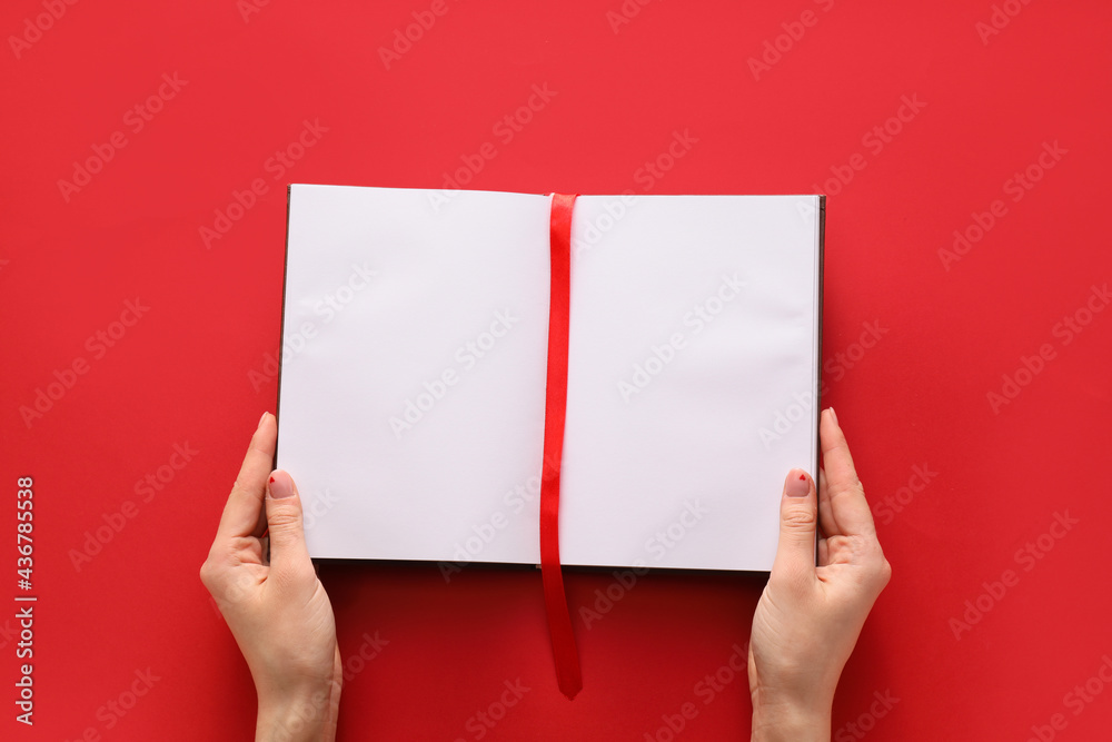Female hands and blank book with bookmark on color background Female hands and blank book with bookmark on color background