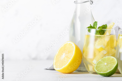 Bottle and glass of tasty cold lemonade on light background, closeup