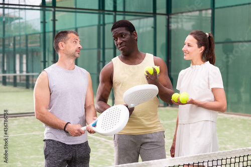 Group of three paddle tennis players standing on court and talking friendly about match © JackF