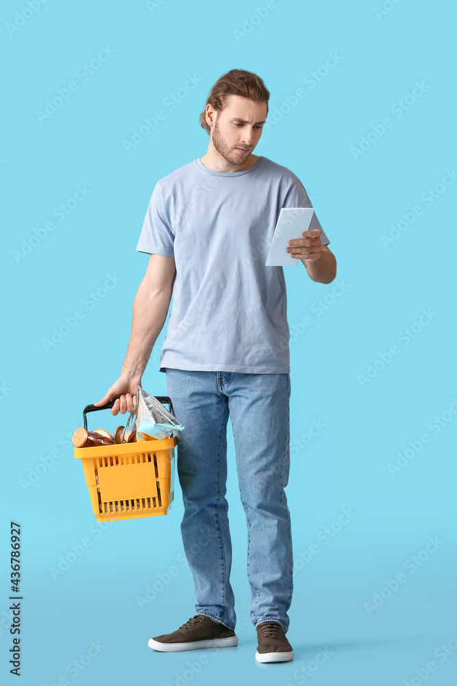 Young man with shopping basket and list of products on color background Young man with shopping basket and list of products on color background