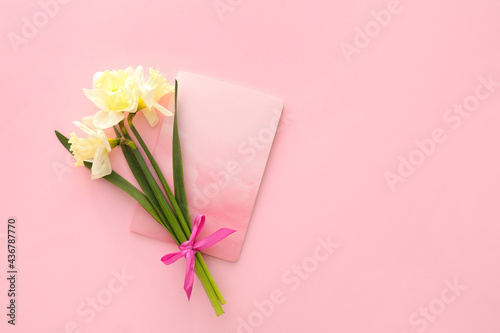 Beautiful daffodils and notebook on color background