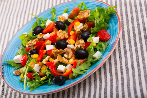 Healthy arugula salad with fresh vegetables, soft cheese, strawberry, walnuts and corn kernels served on colored ceramic plate