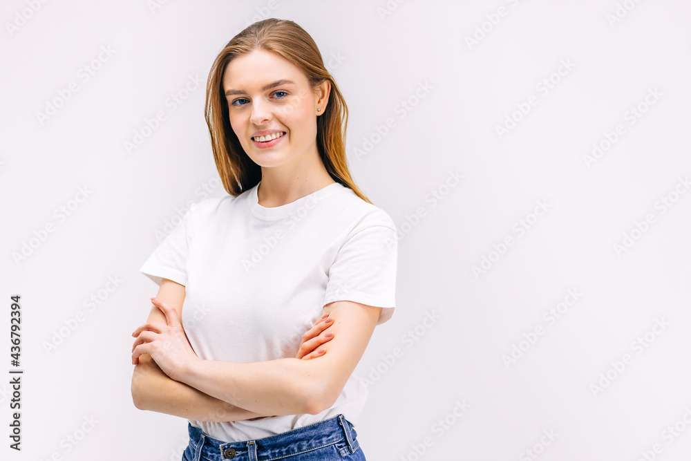of attractive 20s woman wearing white plain t-shirt folds arms smiling confidently isolated on white gray background in studio. Sincere emotions. of attractive 20s woman wearing white plain t-shirt folds arms smiling confidently isolated on white gray background in studio. Sincere emotions.