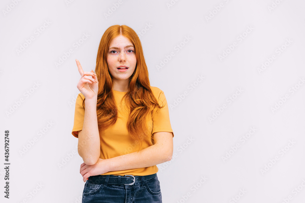 Close up portrait of charming young woman in orange t-shirt pointing with finger up, has an idea, on gray background Close up portrait of charming young woman in orange t-shirt pointing with finger up, has an idea, on gray background
