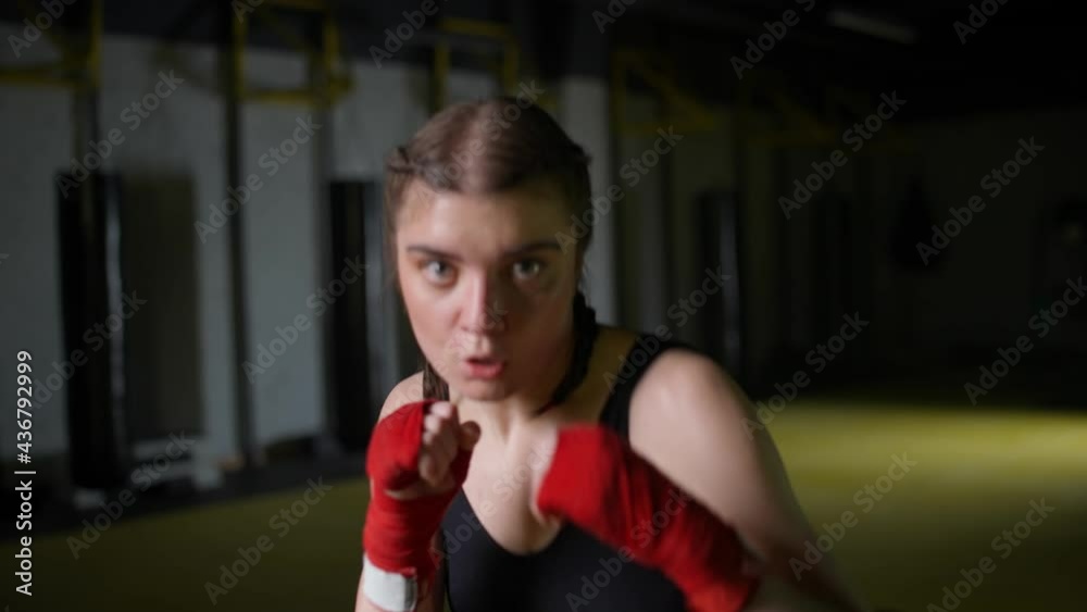 Female fighter trains his punches, training in the boxing gym, young woman looks at the camera and trains a series of punches, front view. Female fighter trains his punches, training in the boxing gym, young woman looks at the camera and trains a series of punches, front view.