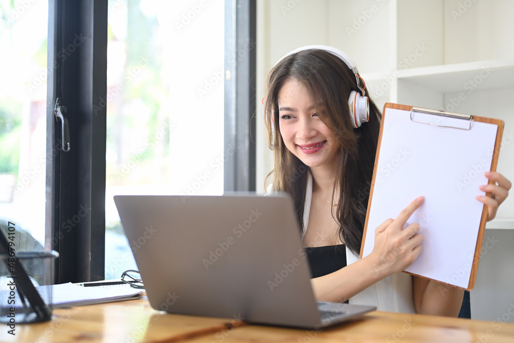 Businesswoman wearing headphone having video call and discussing work with her colleagues on laptop. Businesswoman wearing headphone having video call and discussing work with her colleagues on laptop.