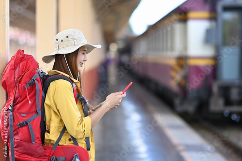 Young asian woman backpacker tourist using smart phone and standing in train station.