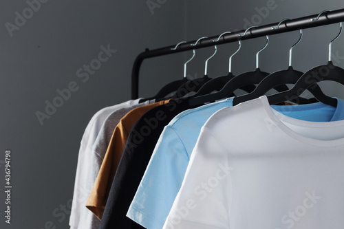 T-shirts of neutral colors on black hanger against gray wall