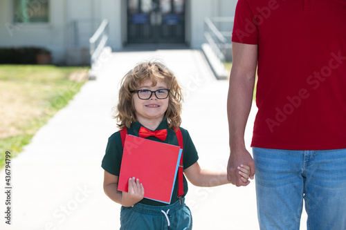 Father supports and motivates son, holding hand outdoors, back to school. Kid nerd going to primary school. photo