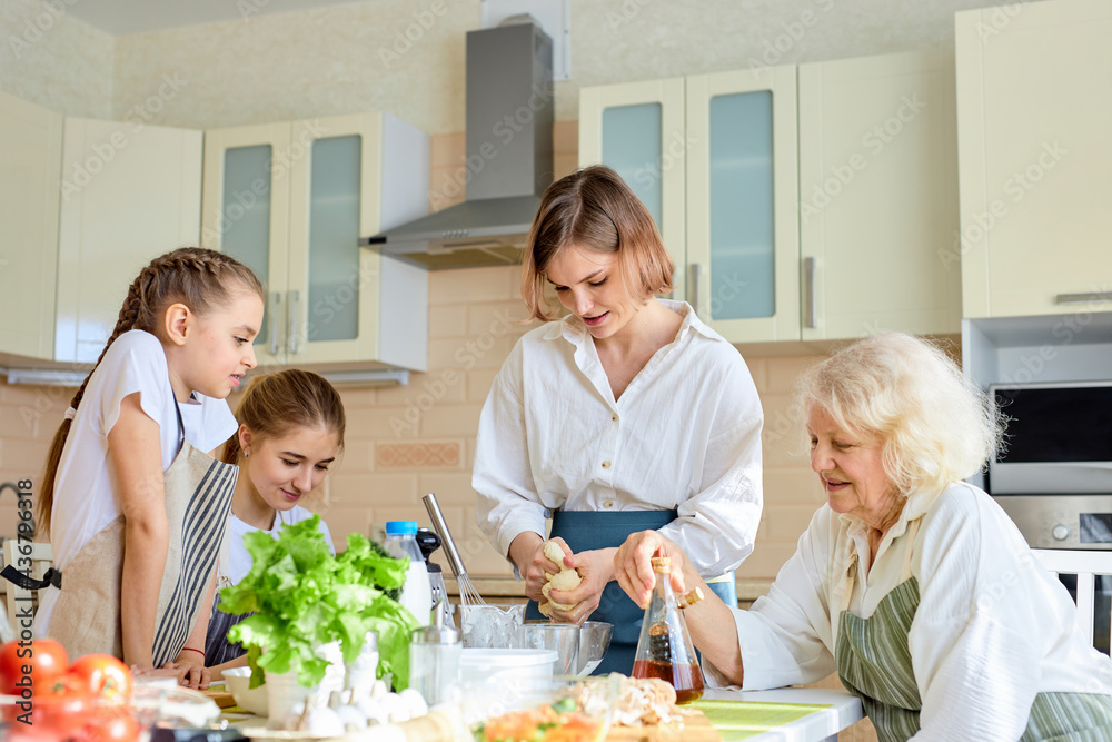 Young woman making dough, teaching children to cook, going to make pizza, at home. Different generations females having talk, spending weekends together, looking at process of cooking