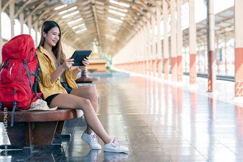 Young female backpacker using tablet searching destination to go while sitting at railway station.