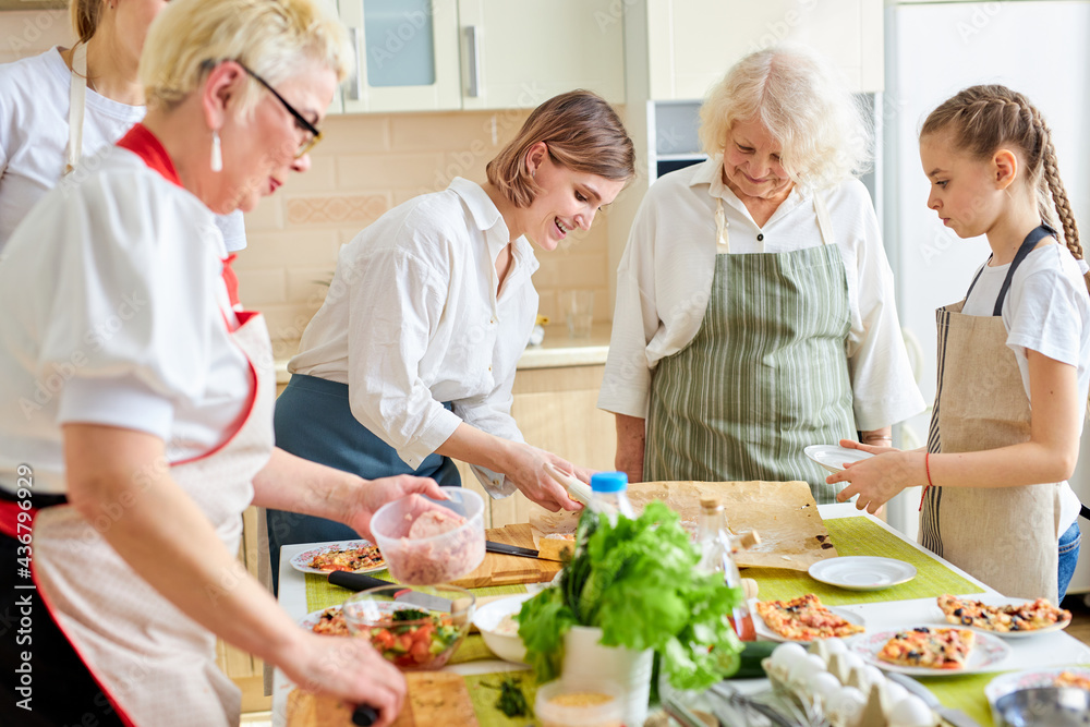 friendly family members, children and adults make pizza for family, add ingredients, copy space and lifestyle, culinary concept. Side view on caucasian happy senior ladies and granddaughters in apron friendly family members, children and adults make pizza for family, add ingredients, copy space and lifestyle, culinary concept. Side view on caucasian happy senior ladies and granddaughters in apron