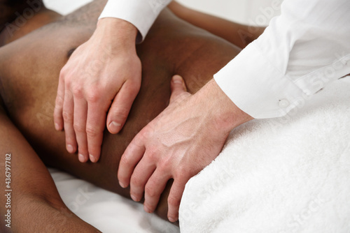 Close up of therapist hands doing visceral massage on african male abdomen on white background, copy space