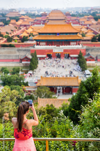 china summer travel. Woman tourist taking pictures with mobile phone of aerial view of imperial palaces, old temples, the forbidden City in Beijing, china. Jingshan Gongyuan park. photo