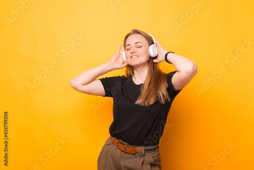 Photo of cheerful woman listening music at white wireless headphones over yellow background