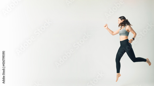 Photo of woman in sportswear jumping over white background with copyspace
