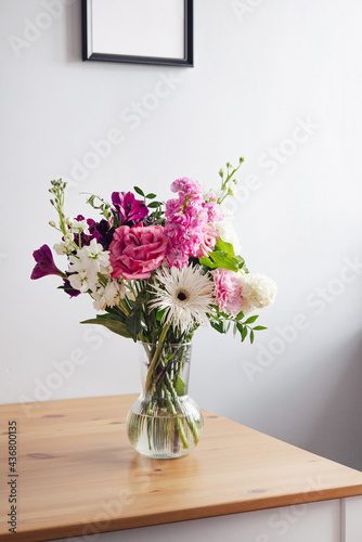 Pink and pastel white flowers in Modern glass vase on wooden table on gray wall background