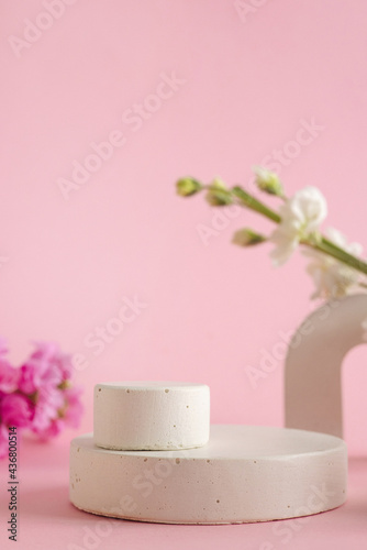 Empty podium for presentation of cosmetic products. Pastel flowers on pink background