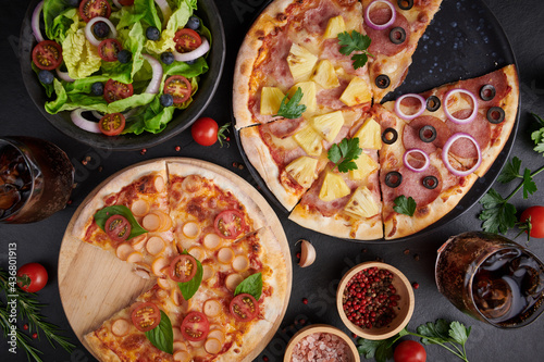Family or friends having pizza party dinner. Flat-lay of people clinking glasses with drink over rustic dark stone table with various kinds of Italian pizza, top view. Fast food lunch, celebration