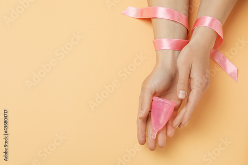 Female hands with ribbon hold menstrual cup on beige background © Atlas