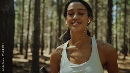 Mixed race female running in forest exercising in nature listening to music with earphones 