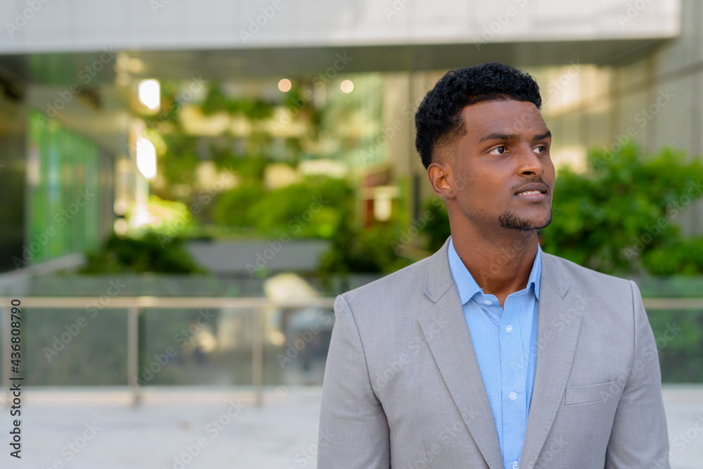 Portrait of handsome young black African businessman thinking outdoors
