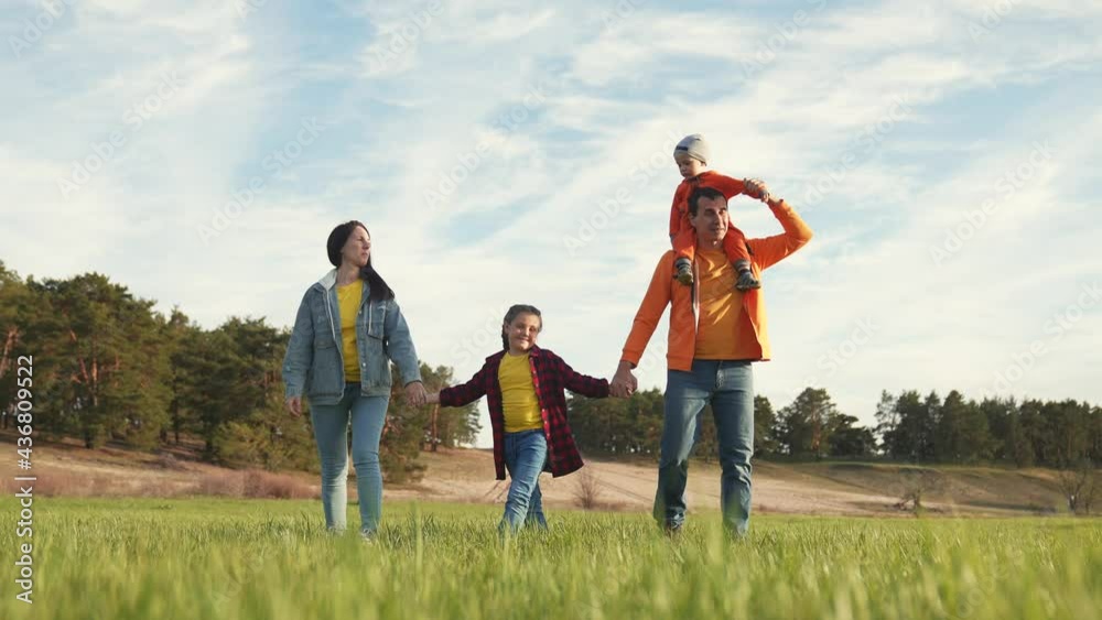 Happy family is walking on green grass. Mom dad and girl with toddler in park at sunset. Happy family walking in park at sunset. Mom dad girl and baby on green grass. Happy family concept at sunset Happy family is walking on green grass. Mom dad and girl with toddler in park at sunset. Happy family walking in park at sunset. Mom dad girl and baby on green grass. Happy family concept at sunset